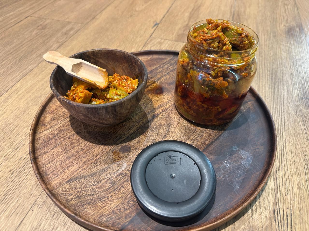 A wooden tray with a bowl of pickle, a wooden spoon and an open jar